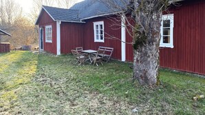 A red building with a sloped roof, a small porch with a table and chairs, and a tree in front. - Charming Old Cottage in Scenic Southern Småland, Just Outside Markaryd | SE07057 (Markaryd)