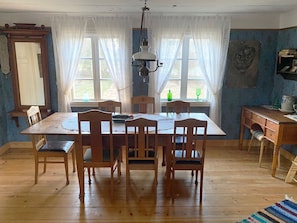 Ein Esszimmer mit Holztisch, Stühlen, einer Chandelier und einem Fenster mit Vorhängen.