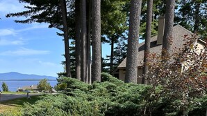 A landscaped garden with various flowering plants and a view of a body of water in the background. - Lake Access-Pool-Beach-Tennis-Fireplace-Sunroom (Gilford)