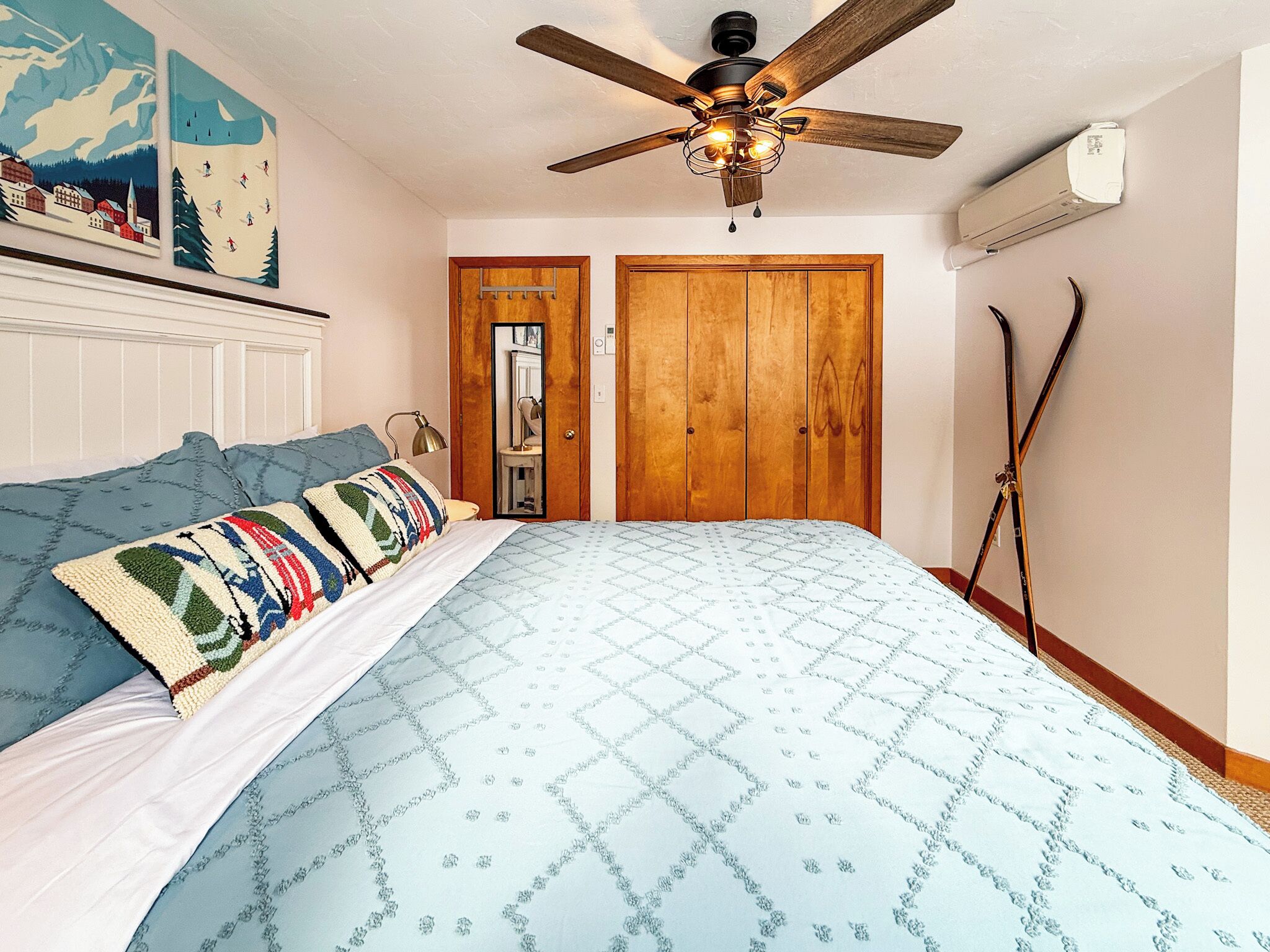A bedroom with a bed, a ceiling fan, a wooden wardrobe, and a mirror.