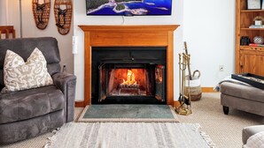 A cozy living room with a fireplace, a mounted TV, and a comfortable sofa. - Lake Access-Pool-Beach-Tennis-Fireplace-Sunroom (Gilford)