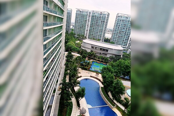 A high-rise building with multiple balconies, a swimming pool, and surrounding greenery.