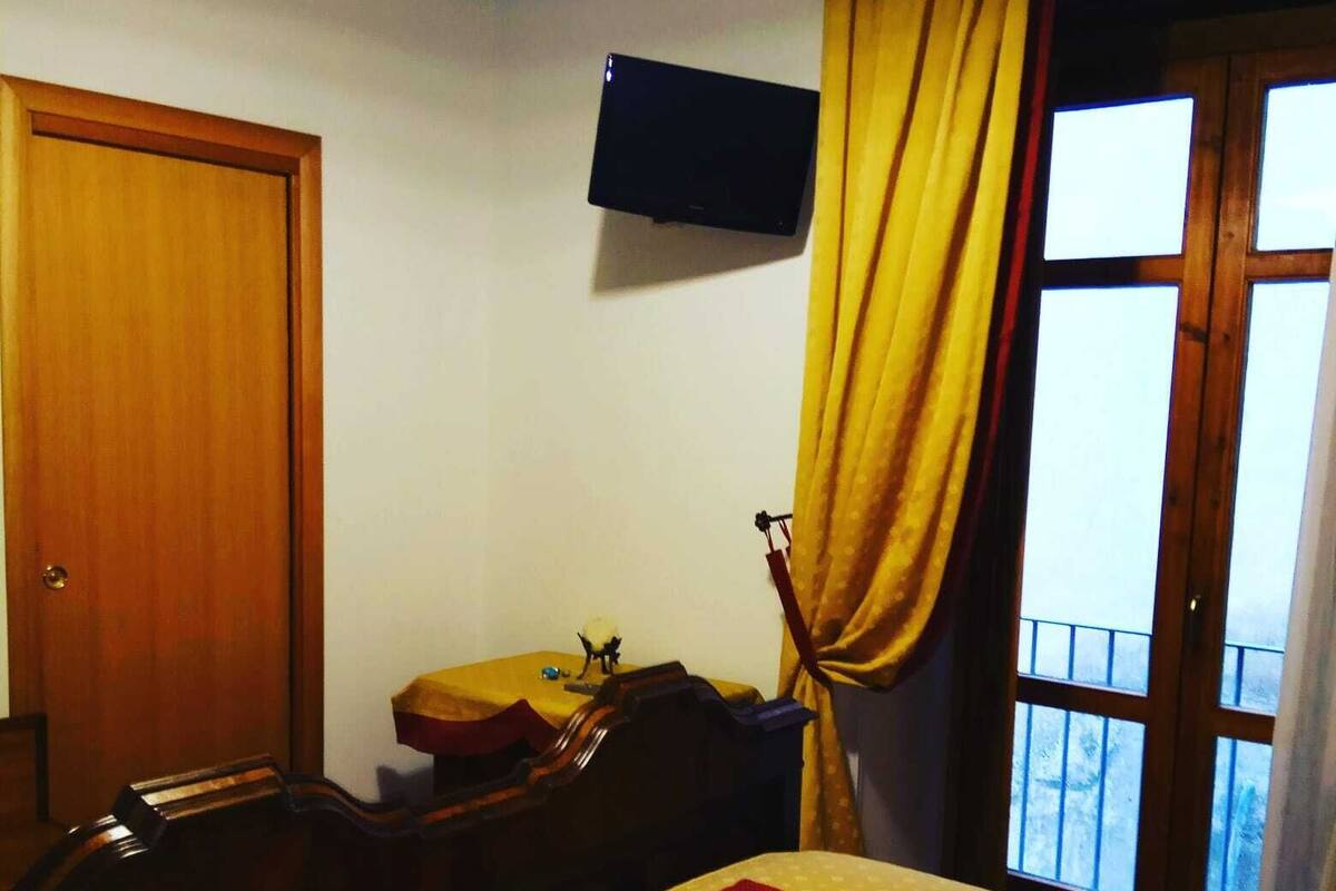 Une chambre d’hôtel comprenant un lit, un bureau, une chaise, un téléviseur fixé au mur et une fenêtre avec des rideaux.