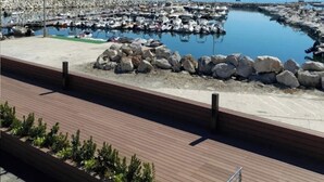 Un puerto deportivo con barcos amarrados, una costa rocosa y un cielo azul despejado.