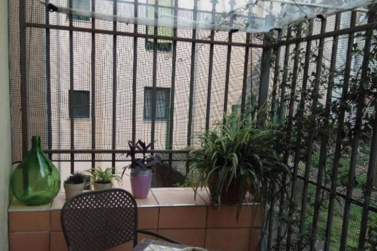 Un petit balcon avec une table carrelée et deux chaises, entouré d’une clôture en métal et agrémenté de plantes en pot.