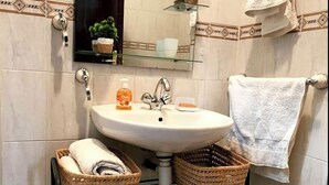 A bathroom with a white sink, a mirror, two wicker baskets, a towel rack, and a small shelf with a plant. - Charming 2-bedroom apartment with AC, WiFi in delightful Marrakech (Marrakech)