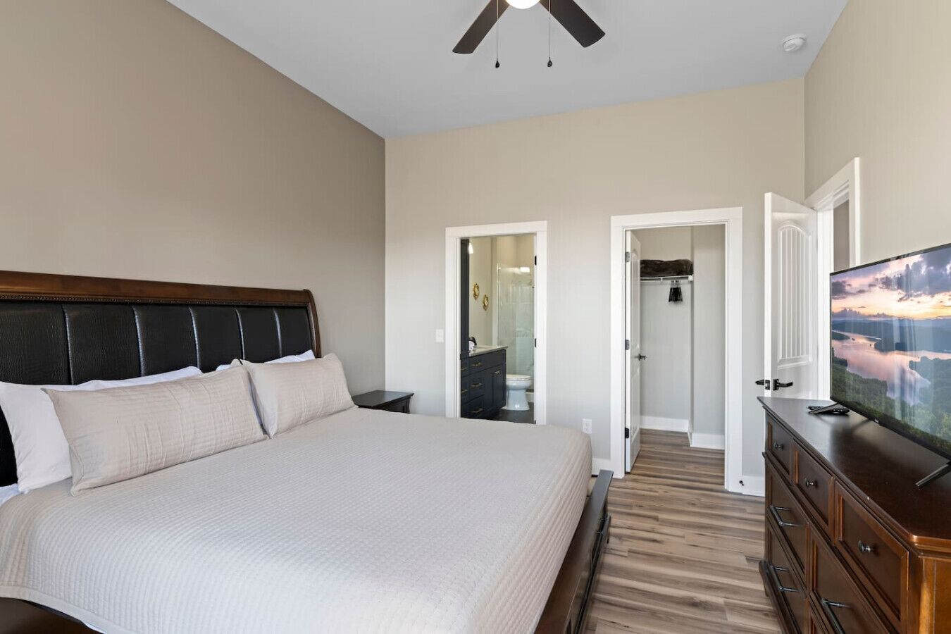 Un dormitorio con una cama grande, televisión, ventilador de techo y vestidor.
