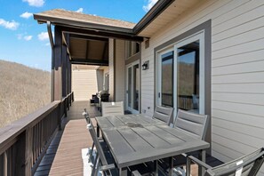 A covered deck with a table and chairs, a sliding glass door, and a view of the surrounding landscape.