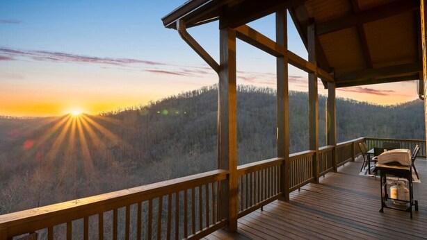 Una terraza de madera con vistas a una colina boscosa al atardecer.
