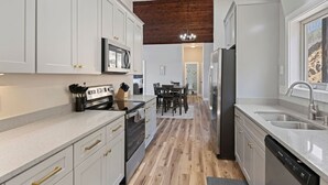 A modern kitchen with white cabinets, a wooden floor, and a dining area in the background.