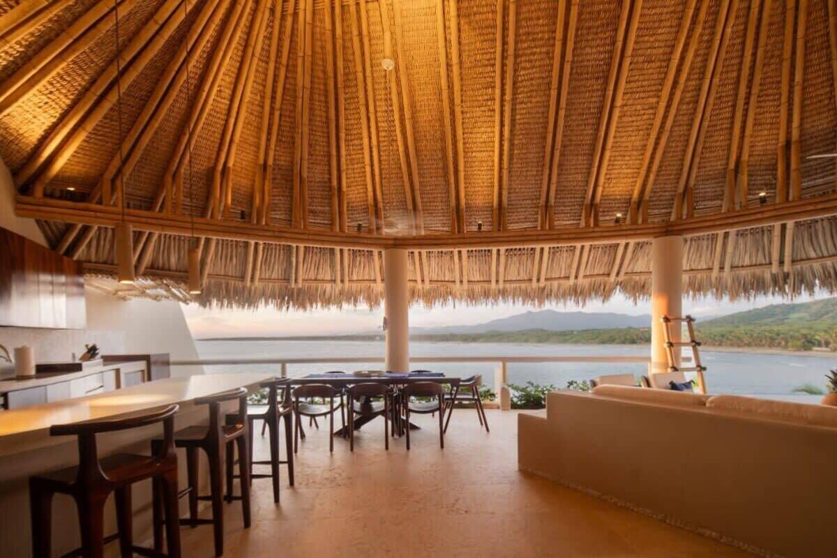 A dining area with a thatched roof, a view of the water, and a table set for four.