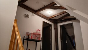 Una habitación con vigas de madera a la vista, una cama, una estantería con objetos y dos puertas.