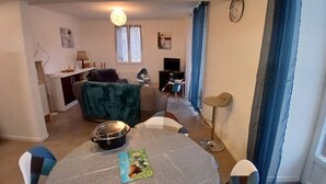 Una sala de estar con una mesa redonda, un sofá, una televisión y una zona de cocina al fondo.