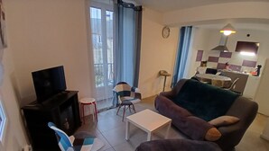 Una sala de estar con un sofá, sillas, una mesa de centro, un televisor y una zona de cocina con estufa y armarios.