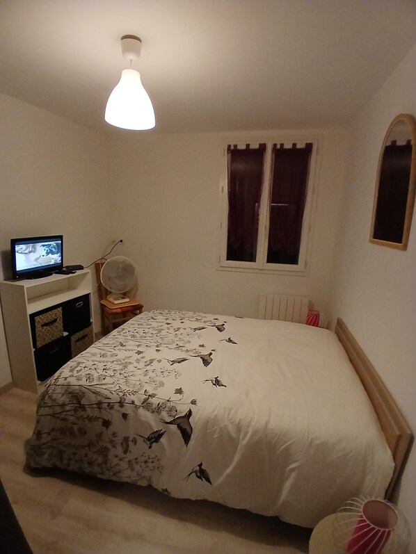 A bedroom with a bed, a desk with a computer, a window with curtains, and a radiator. - Charming T4 duplex in the heart of the village (Saint Geniez d'Olt et d'Aubrac)