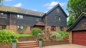 A two-story house with a brick facade, a red garage door, and a well-maintained front yard with steps leading to the entrance. - Traditional English House (Brighton and Hove)