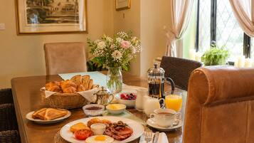 A breakfast setting with croissants, eggs, bacon, toast, and fruit on a table.