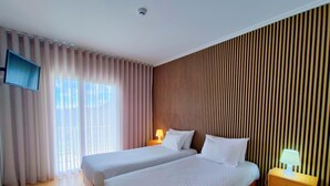 Habitación de hotel con dos camas, un televisor fijado a la pared, una ventana con cortinas y un revestimiento de pared de madera.
