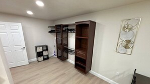 Una stanza con pavimento in legno, una porta bianca, un armadio con ripiani, un tavolino e un elemento decorativo a parete.