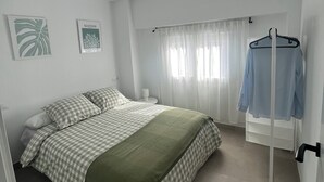 A bedroom with a bed, a hanging clothes rack, a nightstand, and a window with curtains.