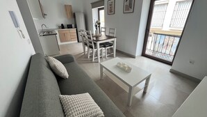 A modern living room with a grey sofa, a white coffee table, and a dining area with a white table and chairs.