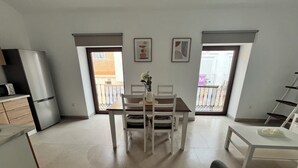 A modern kitchen with a refrigerator, microwave, and wooden cabinets. There is a dining area with a table and chairs, and a balcony with a view.