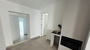 A spacious hallway with a modern kitchen area featuring a built-in oven and a small countertop with a bowl and flowers.