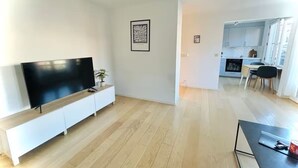 Un salon moderne avec un téléviseur à écran plat posé sur une console blanche, une œuvre d’art encadrée accrochée au mur et un plancher en bois.