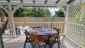 A covered patio with a round table set for dining, surrounded by chairs, under a white lattice structure.