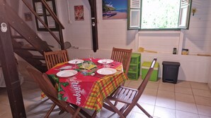 A dining area with a table set for four, wooden chairs, a staircase, a window with shutters, and a painting on the wall.