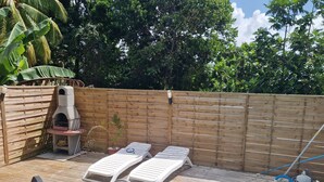 A poolside area with a wooden deck, lounge chairs, a barbecue grill, and a pool.