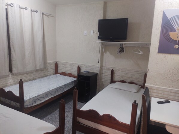 A small, compact room with two single beds, a desk, a chair, a television mounted on the wall, and a power outlet. - POUSADA NASCENTE DO SOL (Macae)