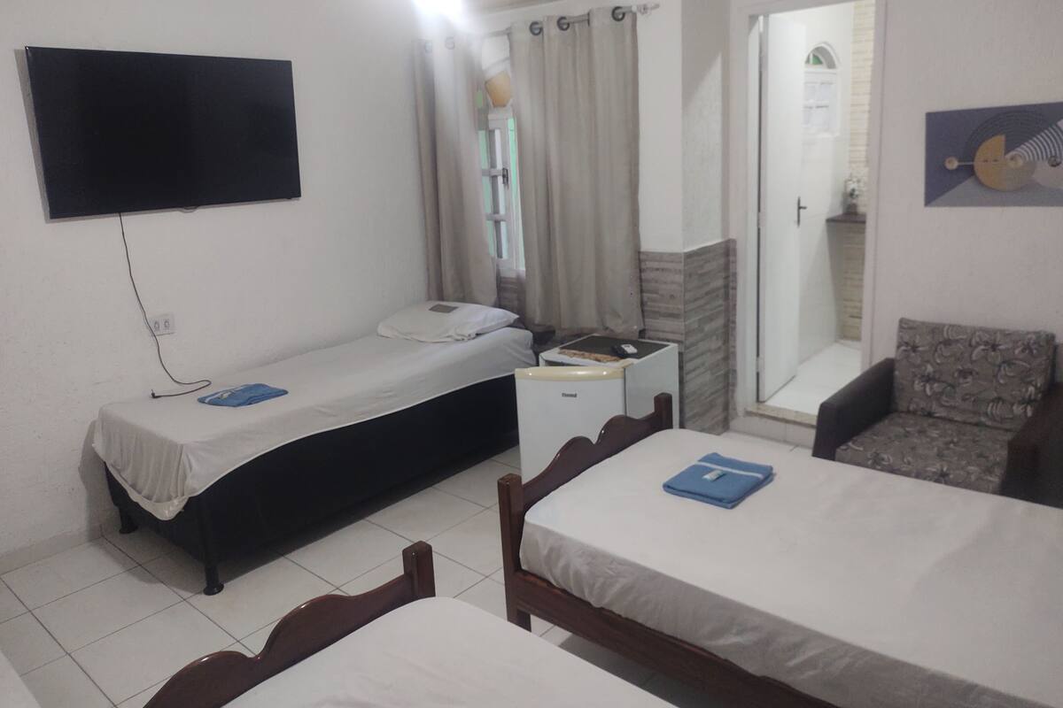 Una habitación con dos camas individuales, un televisor montado en la pared, una mesita pequeña y una silla.