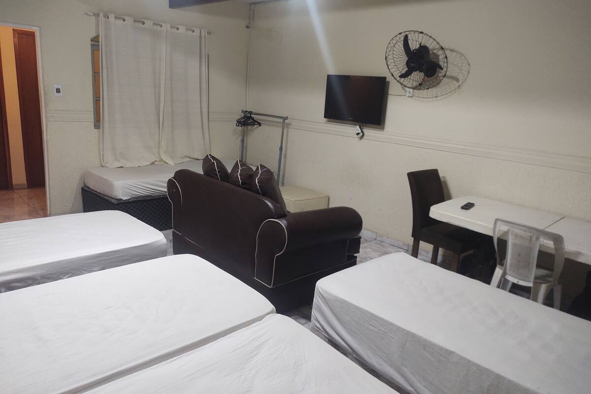 Habitación de hotel con dos camas individuales, un sofá, un escritorio, una silla, un televisor y un ventilador de pared.