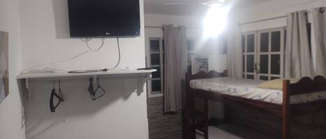 A room with a bunk bed, a desk with a flat-screen TV, a ceiling fan, and a window with curtains.