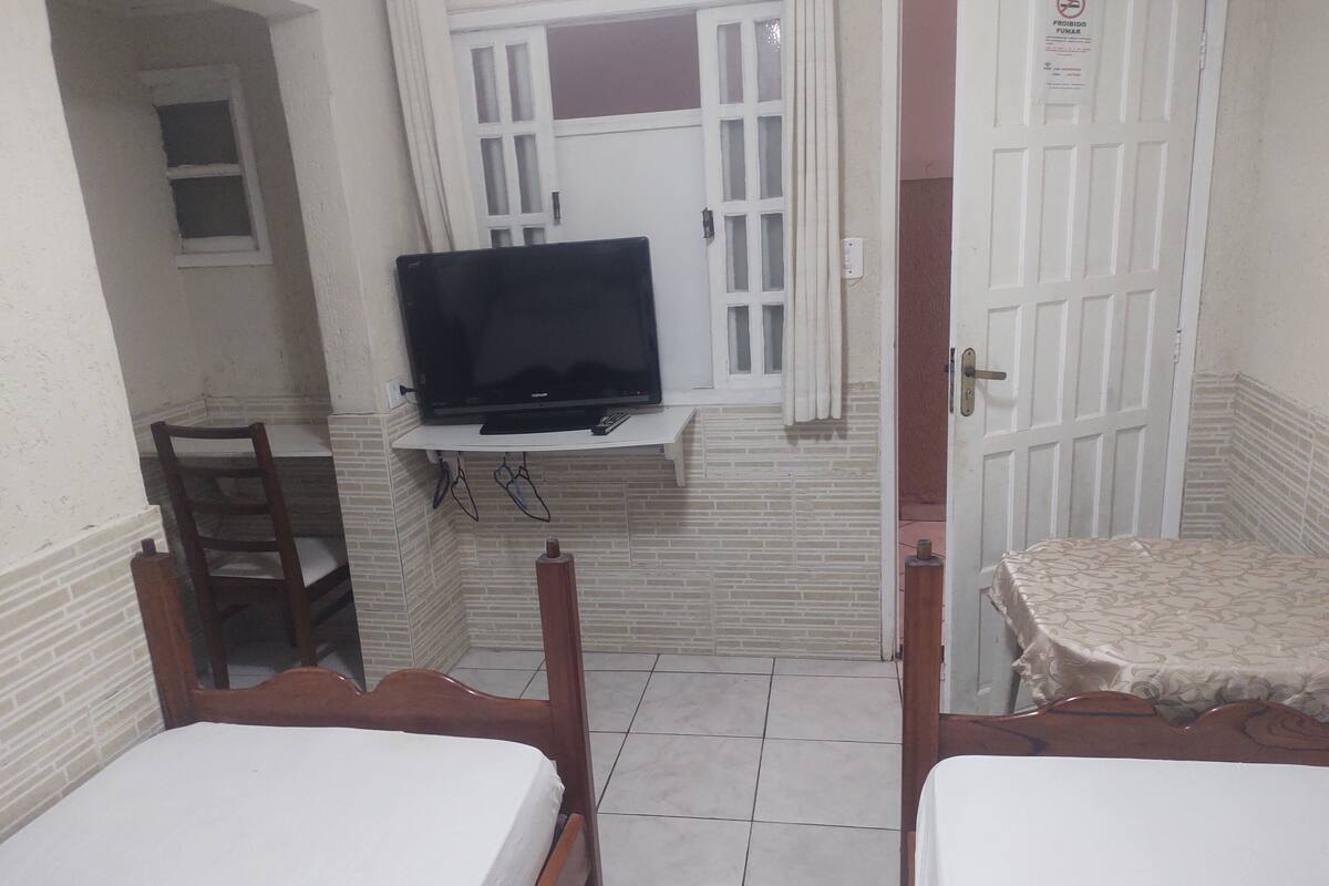 Una habitación pequeña con dos camas, un televisor en un estante y una puerta con un letrero.