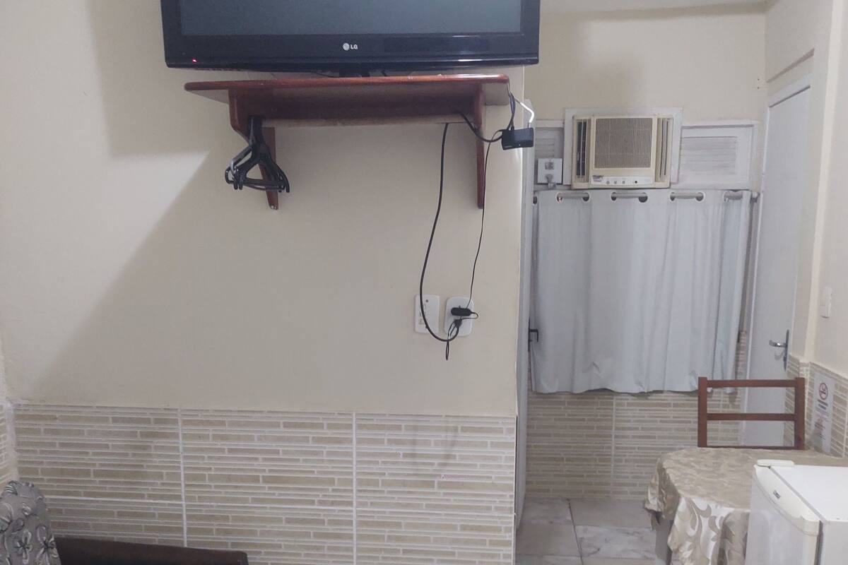Habitación de hotel con televisor montado en la pared, una mesita pequeña, un sofá y un baño visible a través de una puerta abierta.