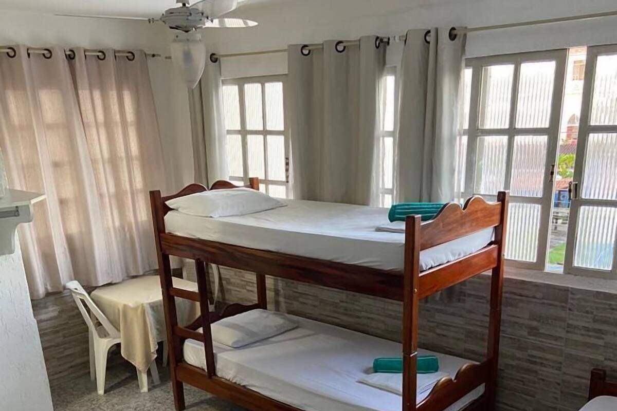 Habitación con literas, un ventilador de techo, una mesita pequeña y una silla.