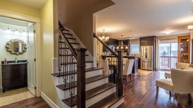A spacious living room with a wooden staircase, a dining area, and a kitchen.