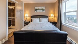 A bedroom with a large bed, two bedside lamps, a window with a view, and a closet with a mirror.