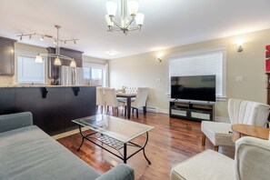 Una sala de estar moderna con una mesa de centro de vidrio, un sofá, un televisor y un comedor con sillas.