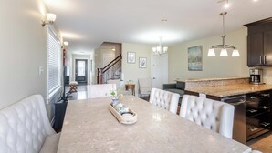 A modern kitchen with a marble countertop, stainless steel appliances, and a dining area with a marble table and white upholstered chairs.