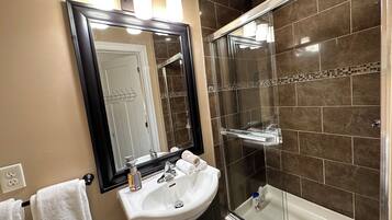 Un baño con un lavabo blanco, un espejo, una ducha con puerta de cristal y una pared con azulejos.