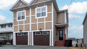 A two-story residential building with a beige exterior and white trim, featuring two garage doors and a small front porch.