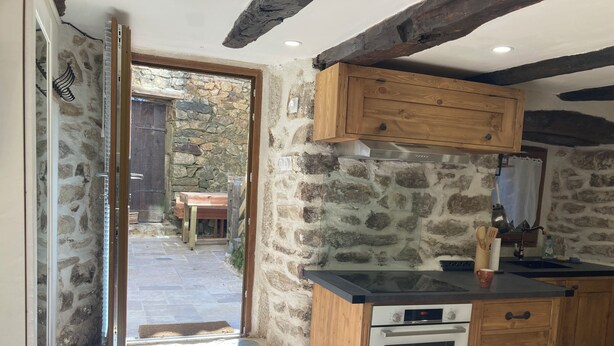 A rustic kitchen with stone walls, wooden cabinets, and a built-in oven. - Entre Eaux et Roches - 5-person gite in character Ardèche house (Beaumont)