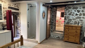 A bedroom with a bed, a wooden dresser, a shower with a glass door, and a stone wall. - Entre Eaux et Roches - 5-person gite in character Ardèche house (Beaumont)