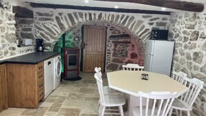 A rustic kitchen with a stone wall, wooden cabinets, a washing machine, and a dining table with white chairs. - Entre Eaux et Roches - 5-person gite in character Ardèche house (Beaumont)