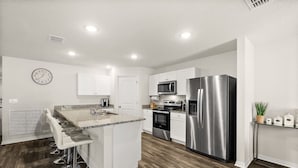 A modern kitchen with white cabinetry, stainless steel appliances, and a central island with bar stools. - Private Pool 4BR | Sleeps 10 + Near Beach (Palm Coast)