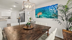 A modern kitchen with white cabinets, a stainless steel refrigerator, and a dining area with a wooden table and white chairs. - Private Pool 4BR | Sleeps 10 + Near Beach (Palm Coast)