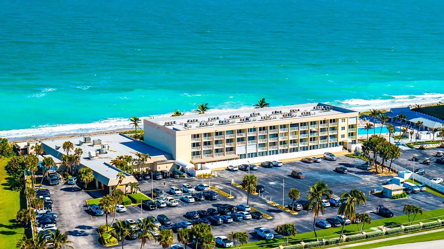 Un hôtel à plusieurs étages doté d’un parking, situé près d’une plage aux eaux turquoise et cristallines.
